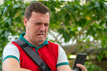 Confused cringe businessman is unpleasantly shocked by what he saw on screen mobile phone, crisis, pay debt. Disgusted and overwhelmed millennial man stares at screen of smart phone.