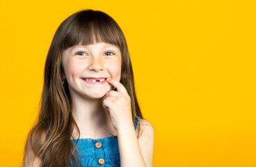 The little girl's front tooth fell out, toothless smile of a first grader. Isolated on yellow background