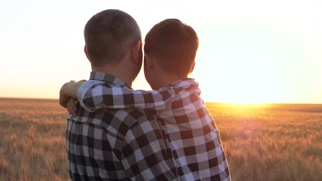 A happy child hugs his father. Dad holds his son in his arms. A family looks at the sunset in a wheat field. The concept of a happy family, grain export and import, agriculture.