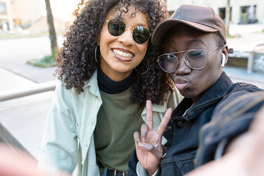 two young african american women taking selfie, hip hop street style, friends using app mobile to connect to social media, positive image and gesture of victory with the hand, copy space