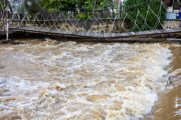A low view of the river flowing violently past a broken wooden bridge.