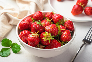 Strawberries in a white bowl on a light background. Side view, close-up. Healthy food