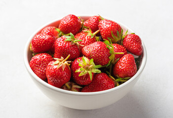 Strawberries in a white bowl close-up on a light background. Side view.