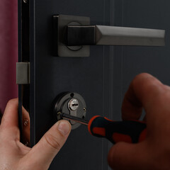 Installation of a door lock, a carpenter installs a door lock in a door, work close-up.