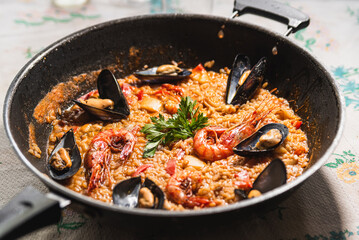 Traditional spanish seafood paella or arroz caldoso inside black pan with shrimps, mussels, clams and parsley. Homemade traditional paella inside paellera pot at home with table cloth