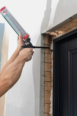 a man uses a spray gun with his hand and fills the gap with construction foam between a new wooden door and a wall. - obrazy, fototapety, plakaty