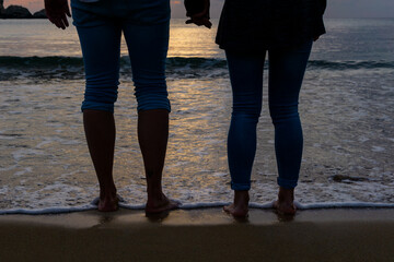 Detail of the legs of two unrecognizable young women on the seashore at sunset.