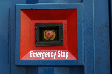 Red Emergency stop button placed on the wall of blue container of electric power pack. Button is in...