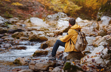 Travel and road trip concept at autumn. Adventure and active lifestyle in nature. Tourist hiking in forest. Caucasian man in yellow jacket walks in woods.