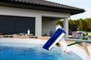 Cleaning the home pool in the garden with a brush, cleaning and maintenance of the home pool.