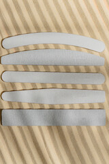 Different types and shapes of nail files on sandy background with hard shadows. Mockup.