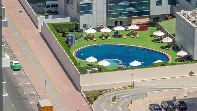 Rooftop swimming pool viewed from above timelapse, Aerial top view at Dubai marina. People swimming and relaxing under umbrellas. Traffic on the road. Dubai, UAE