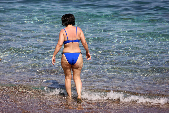 Woman in blue swimsuit going to swim in blue transparent water. Vacation on summer beach