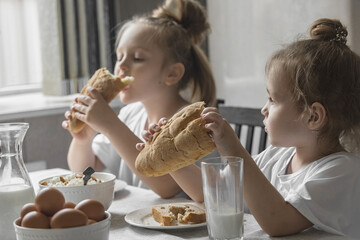 two little girls in white t-shirts have breakfast at home in the kitchen with natural and healthy, homemade products. Proper and healthy nutrition for children at home
