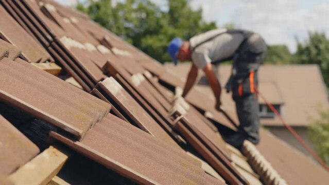 Professional roofer on rooftop in safety harness working with roof tiles.
