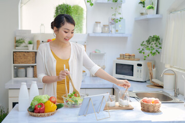 Woman in kitchen preparing vegetables and using tablet