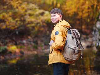 Travel and road trip concept at autumn. Adventure and active lifestyle in nature. Tourist hiking in forest. Caucasian man in yellow jacket walks in woods.