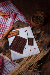 Broken bar of dark bitter chocolate with chilly pepper, red pea pepper, cinnamon flavour on paper,...