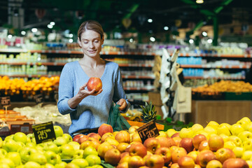 A woman in a supermarket, a buyer chooses an apple fruit, buys and puts an ecological bag in the basket