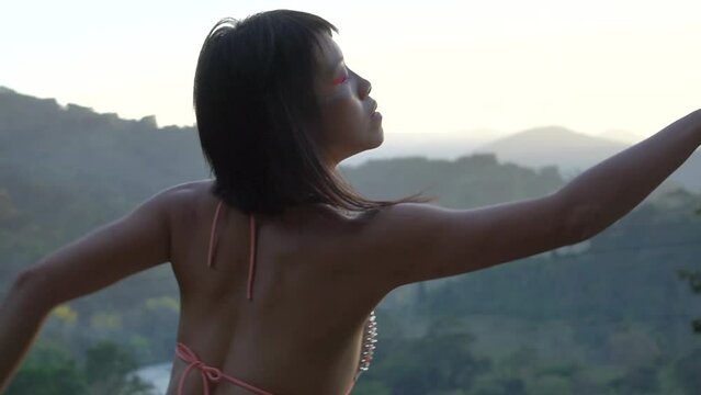 Elegant Asian girl with painted body performing an extatic dance in the tropical valley at sunset time. Mountains Oaxaca