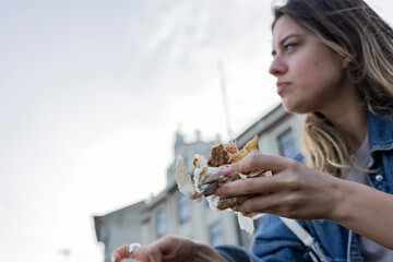 Young woman eating grilled fish sandwich. The focus is on her hand. Low angle photograph.