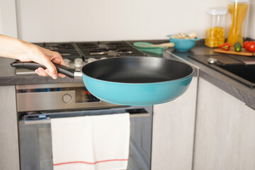 The hand of a young woman holds a frying pan on the background of the kitchen.