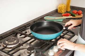 Young woman holding a new frying pan in her hands on the background of the kitchen