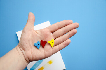 Flatlay horizontal composition hearts of three colors on the arm, red, blue and yellow button  and blank blue background