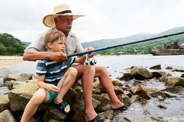 Grandfather fisher in straw hat and little male grandkid enjoying leisure activity use fishing rod