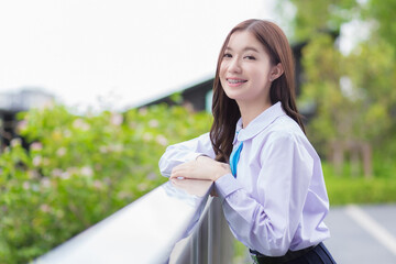 Beautiful high school Asian student girl in the school uniform confidently stands and smiles...