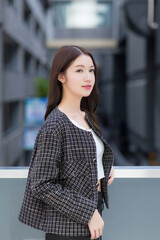Portrait of a beautiful, long-haired Asian female side face in a black pattern coat with braces on teeth standing and smiling outdoors in the city.