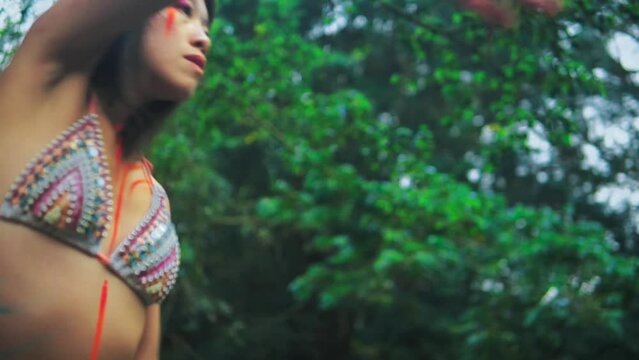 Elegant Asian girl with painted body performing an extatic dance in a lush tropical forest near calm clean pond. 