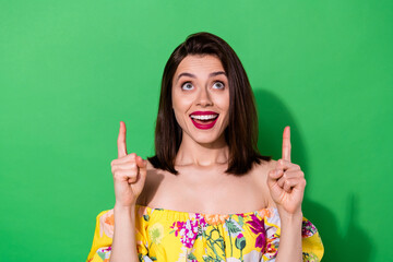 Portrait of positive pretty girl look indicate fingers up empty space ad blank isolated on green...