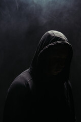Silhouette of bandit in hoodie on black background with smoke - obrazy, fototapety, plakaty