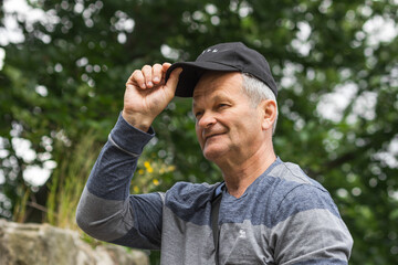 Obraz premium Portrait of smiling caucasian senior man with black baseball cap and casual clothing. Isolated on the nature background.