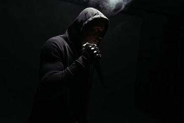Silhouette of african american bandit holding knife on black background with smoke