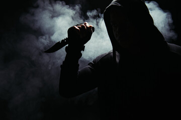 Silhouette of african american bandit in hood holding knife on black background with smoke