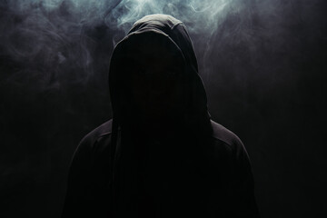Silhouette of hooligan in hood on black background with smoke - obrazy, fototapety, plakaty