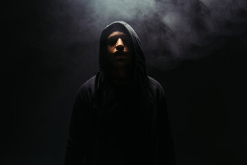 African american hooligan in hoodie standing on black background with smoke - obrazy, fototapety, plakaty