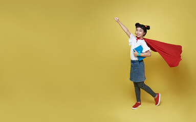 Little child asian girl superhero holding book on yellow background. Girl power hero concept.