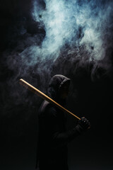 Silhouette of bandit with wooden baseball bat on black background with smoke