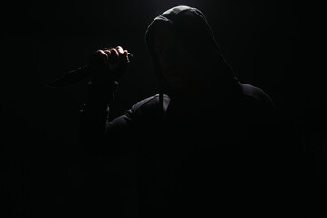 Silhouette of bandit in hoodie holding knife isolated on black