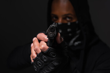 Blurred african american bandit in gloves holding handgun isolated on black