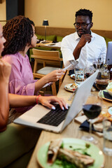 A group of interracial casual businesspeople is sitting in a restaurant on a team building and discussing the project.