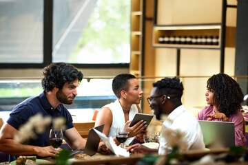 Obraz premium A group of casual businesspeople is sitting in a restaurant for a meeting, discussing a project while having dinner.