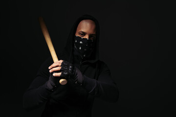 African american hooligan in mask on face and glove holding baseball bat isolated on black