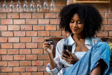 Young woman consumer holding credit card and smartphone buying online at home. Woman shipping...