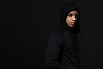 African american hooligan in hoodie looking at camera while standing isolated on black