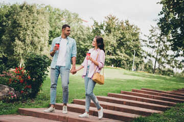 Photo of charming dreamy boyfriend girlfriend wear casual outfits walking stairs drinking beverages enjoying sunny outdoors garden