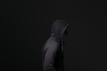 Side view of african american hooligan in hood standing isolated on black - obrazy, fototapety, plakaty